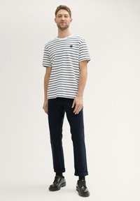 T-shirt à rayures blanches avec des lignes marines, col rond, manches courtes, associé à un pantalon marine foncé et des chaussures en cuir noires.