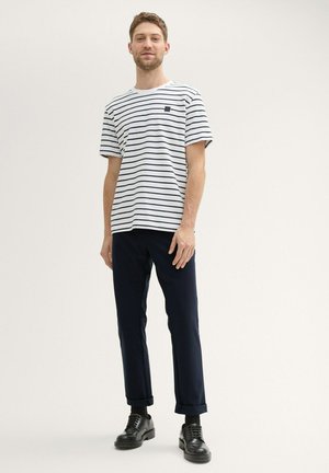 T-shirt à rayures blanches avec des lignes marines, col rond, manches courtes, associé à un pantalon marine foncé et des chaussures en cuir noires.