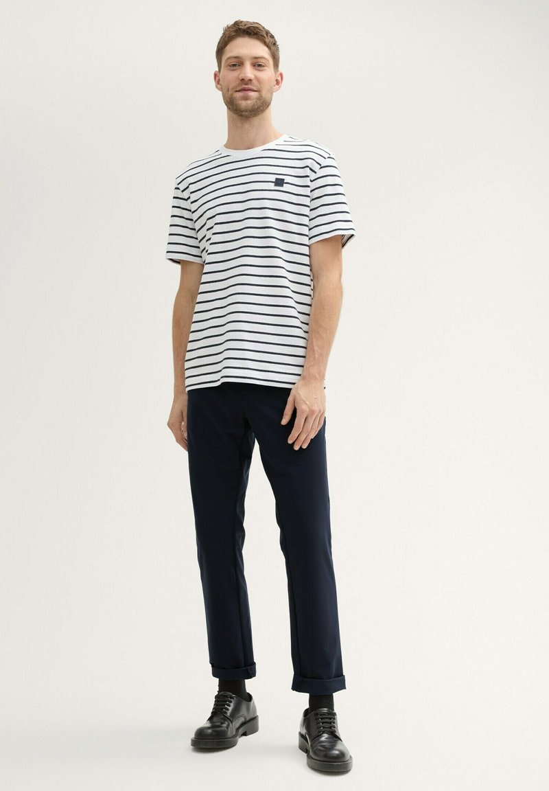 T-shirt à rayures blanches avec des lignes marines, col rond, manches courtes, associé à un pantalon marine foncé et des chaussures en cuir noires.