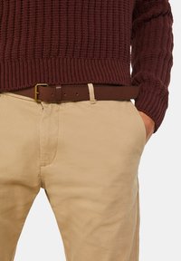Burgundyfärgad stickad tröja med ribbad textur, kombinerad med beige chinos och fäst med ett brunt bälte med ett guldfärgat spänne.