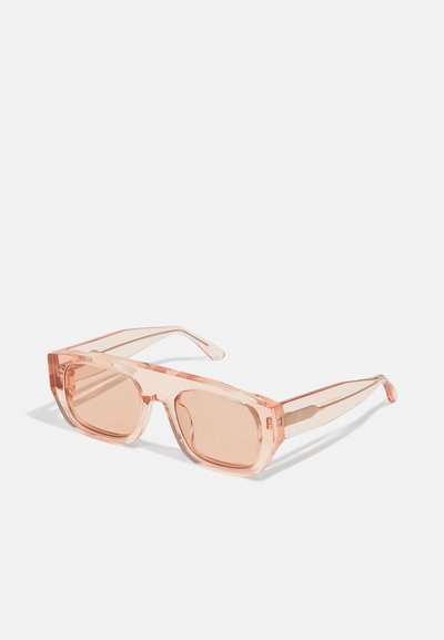 Lunettes de soleil transparentes rose avec des verres rectangulaires et des montures épaisses. Branches fines avec un subtil détail de marque sur la branche.