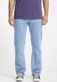 Jean droit bleu clair en denim, avec un design classique à cinq poches, porté avec des baskets noires et blanches.