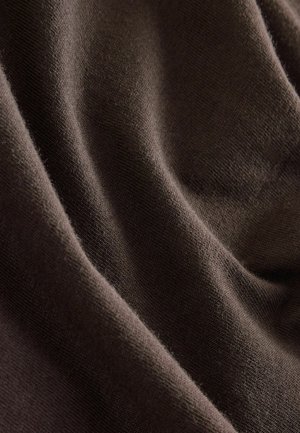 Barna szövet puha, texturált felülettel, finom redőkkel és enyhe rugalmassággal, amely sima, matt minőséget hangsúlyoz.