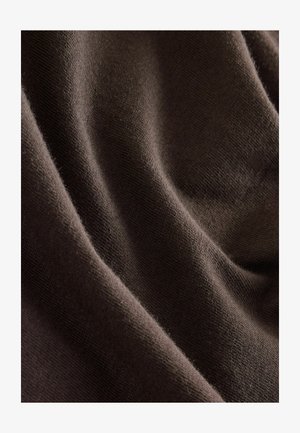 Barna szövet puha, texturált felülettel, finom redőkkel és enyhe rugalmassággal, amely sima, matt minőséget hangsúlyoz.