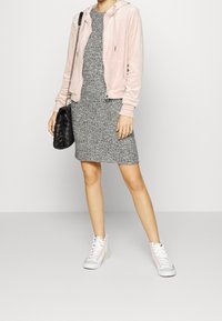 Felpa rosa in velluto con zip sopra un vestito grigio in maglia; abbinata a sneakers bianche alte con dettagli rosa e una borsa a tracolla nera trapuntata.