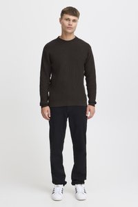 Black ribbed sweater with a round neckline, paired with black pants and white sneakers featuring black stripes. Minimalist design, textured fabric.