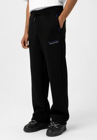 Zwarte sweatpants met een relaxte pasvorm, voorzien van een drawstring tailleband en zijzakken. Blauwe geborduurde tekst op de linkerdij voegt detail toe.