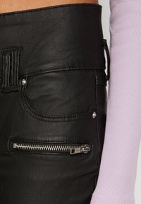 Czarne skórzane spodnie o wysokim stanie, z przednimi kieszeniami i kieszenią na zamek po boku. Teksturowana powierzchnia, srebrne akcenty ze sprzętu.