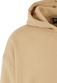 Beige hooded sweatshirt with a soft, textured fabric. Features a large hood and a relaxed fit design. Tag visible at neckline.