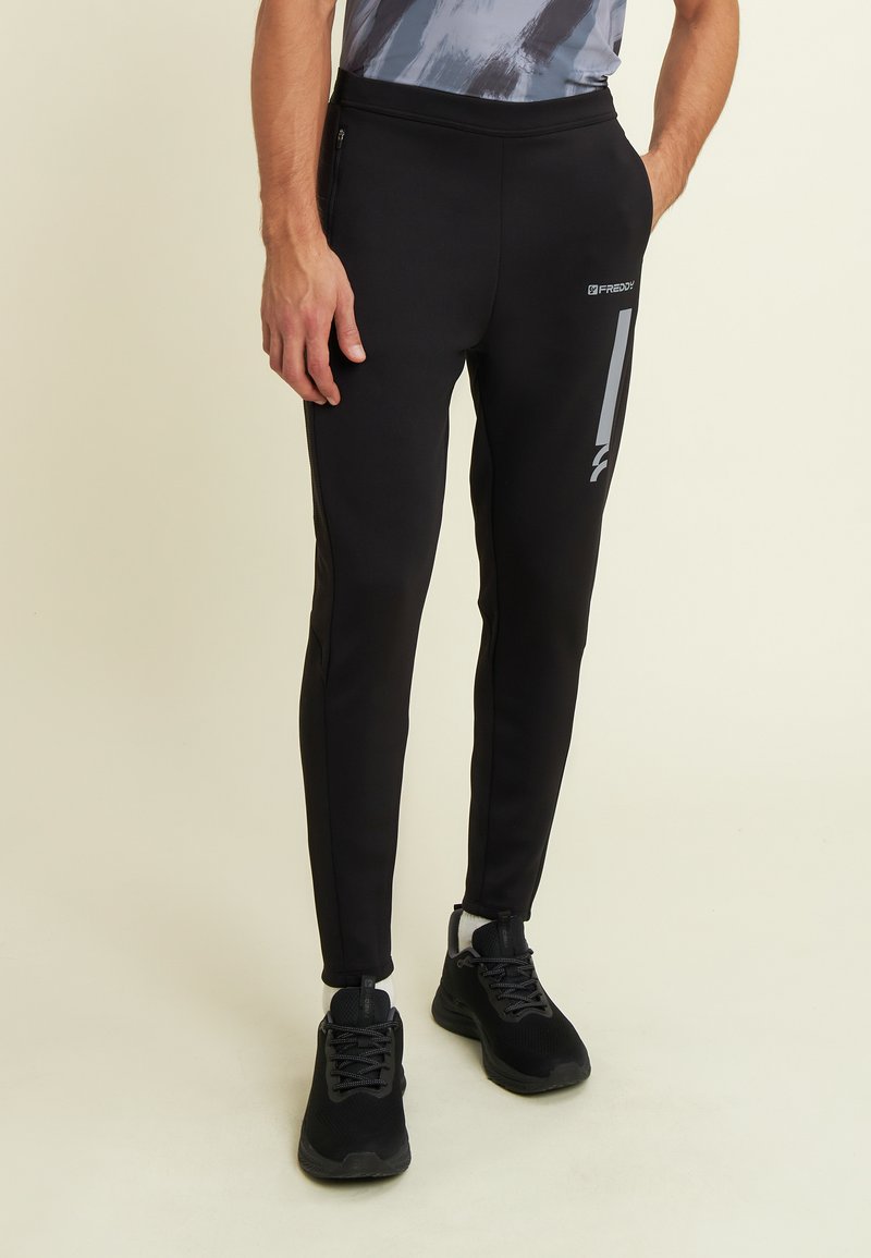 Pantalons de sport noirs ajustés. Comprend une taille élastique, des poches zippées sur les côtés et un accent logo gris. Matériau lisse et extensible.
