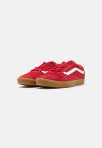 Sneakers in suede rosso con suola in gomma color caramello, con dettagli laterali e lacci bianchi. Design a profilo basso con una finitura texturizzata.
