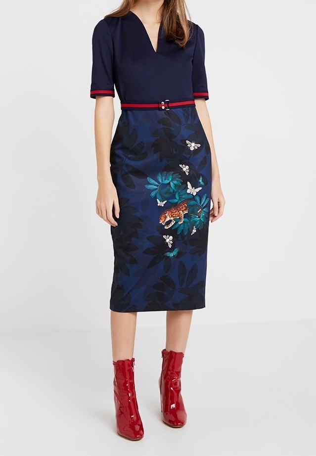 Femme portant une robe bleu marine avec un bord rouge, un motif floral et papillons sur la jupe, et des bottines rouges brillantes.