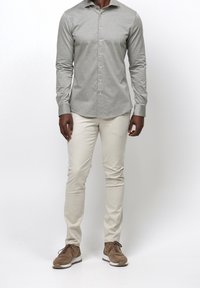 Grå långärmad skjorta med knäppning framtill, kombinerad med krämfärgade snäva byxor och bruna mockaskor. Slät textur, avslappnad design.