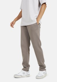 T-shirt oversize grigio chiaro abbinato a pantaloni della tuta beige. I pantaloni della tuta presentano una vestibilità rilassata e tasche, completati da sneakers bianche.