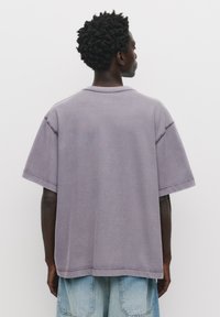 Lilla oversized t-shirt med sænkede skuldre, rå kant og ribbet krave; parret med lyseblå denimshorts.