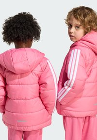 Two children wear puffy, hooded jackets in bright pink with white stripes down the sleeves. The jackets have a quilted texture and reflective accents.