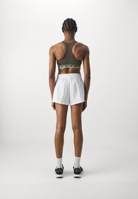 Mørkegrønn sports-bh med lysegrønne detaljer, sammen med hvite shortser. Antrekket har en lav ryggdesign og sorte joggesko.