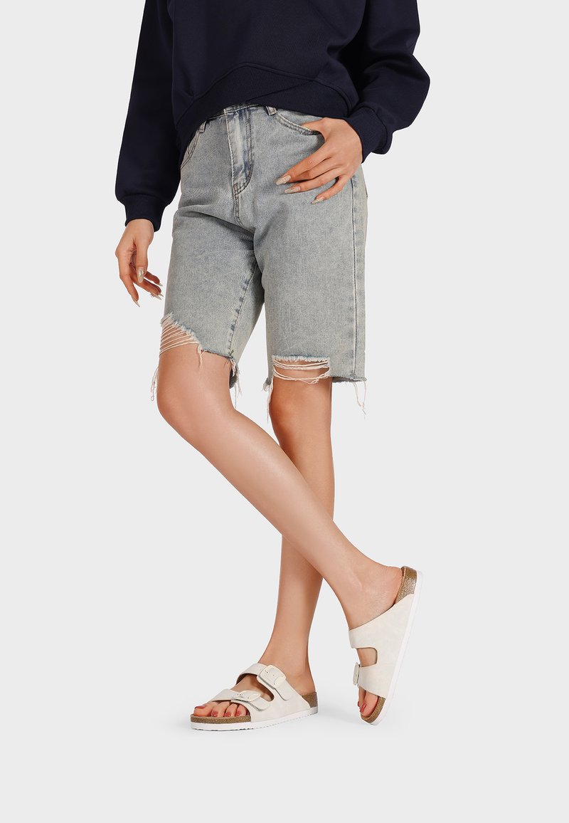 Shorts di denim, azzurri chiari con bordi sfrangiati, abbinati a sandali beige con due cinturini regolabili e una soletta texturizzata.