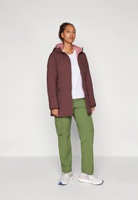 Bordo spalvos gobtuvu striukė su rožine vidine puse, užtrauktukais ir raišteliais. Derinama su žaliais karo stiliaus kelnėmis ir pilkais sportbačiais su oranžiniais akcentais.