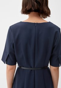 Navy blauwe jurk met korte mouwen, een rechte halslijn aan de achterkant en een zwarte riem die op de taille knelt. Heeft een zichtbare ritssluiting aan de achterkant.