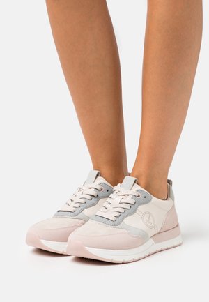 Hellrosa und graue Schnürsneaker, barfuß getragen, vor einem schlichten weißen Hintergrund gezeigt.