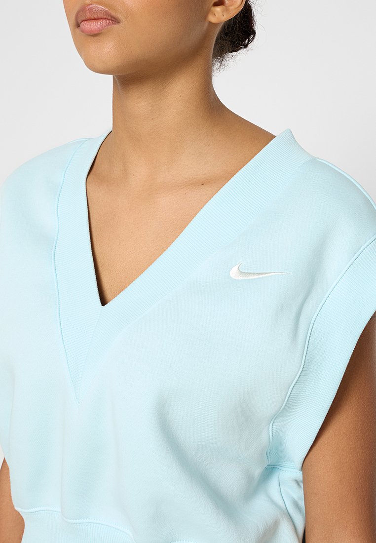 Femme portant un haut sans manches en V de couleur bleu clair avec le logo Nike en blanc sur la poitrine, vue recadrée des épaules à la taille.