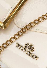 Kabelka Wittchen z lesklé béžové lakové kůže, s zlatým řetízkem a zlatým emblémem na přední straně. Hladká textura s metalickými akcenty.