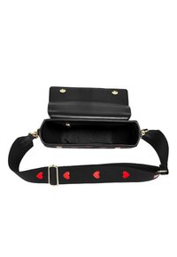 Černá kožená krosbody taška s hladkým povrchem, která má magnetické zavírání a popruh zdobený červenými srdíčky.