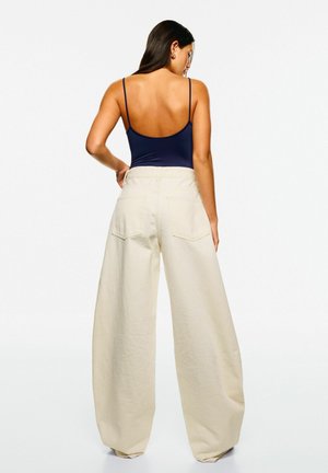 Navy tætsiddende bodysuit kombineret med højtidede, brede cremefarvede bukser. Bukserne har to baglommer og en glat, mat tekstur.