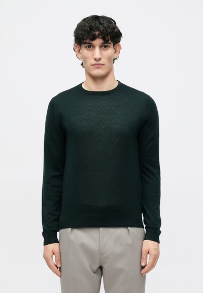Dark green sweater with a textured diamond pattern, round neckline, and long sleeves, paired with light gray trousers.