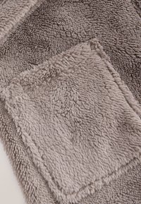 Échantillon de tissu rectangulaire gris doux et duveteux, placé en diagonale sur un fond gris à texture similaire.