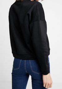 Sweat-shirt noir avec un col rond et des coutures d'épaules tombantes, associé à un jean bleu avec une conception classique à cinq poches.