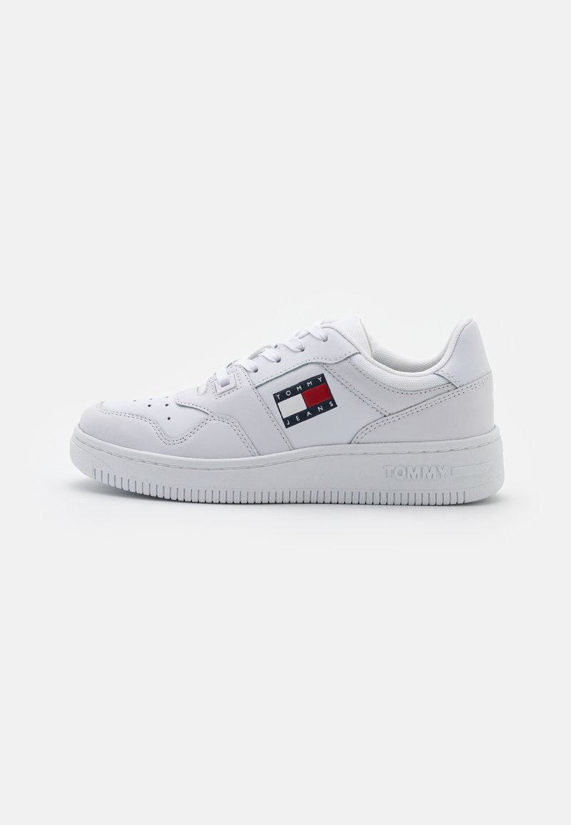 Zapatilla blanca con suave cuero sintético, diseño de cordones, perforaciones en la puntera y un parche con el logo en rojo, blanco y azul en el lateral.