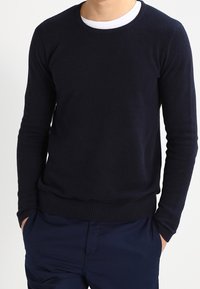 Granatowy sweter z prążkowanej dzianiny z okrągłym dekoltem i długimi rękawami, charakteryzujący się strukturalnym materiałem i dopasowanym dołem, noszony na ciemnych spodniach.