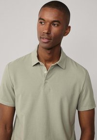 Polo shirt verde chiaro realizzato in tessuto morbido, con colletto, maniche corte e pattina con tre bottoni. Texture liscia e design semplice.