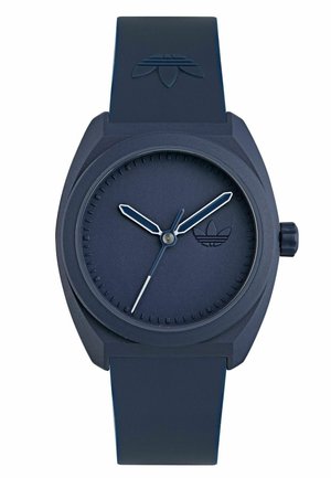 Montre en silicone bleu marine avec un bracelet texturé, un cadran rond minimaliste et des aiguilles des heures et des minutes argentées. Présente un petit logo sur le cadran.