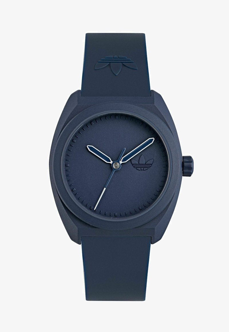 Tamsiai mėlynas silikono laikrodis su tekstūruotu dirželiu, minimalistiniu apvaliu ciferblatu ir sidabriniais valandų bei minučių rodyklėmis. Ciferblate yra mažas logotipas.