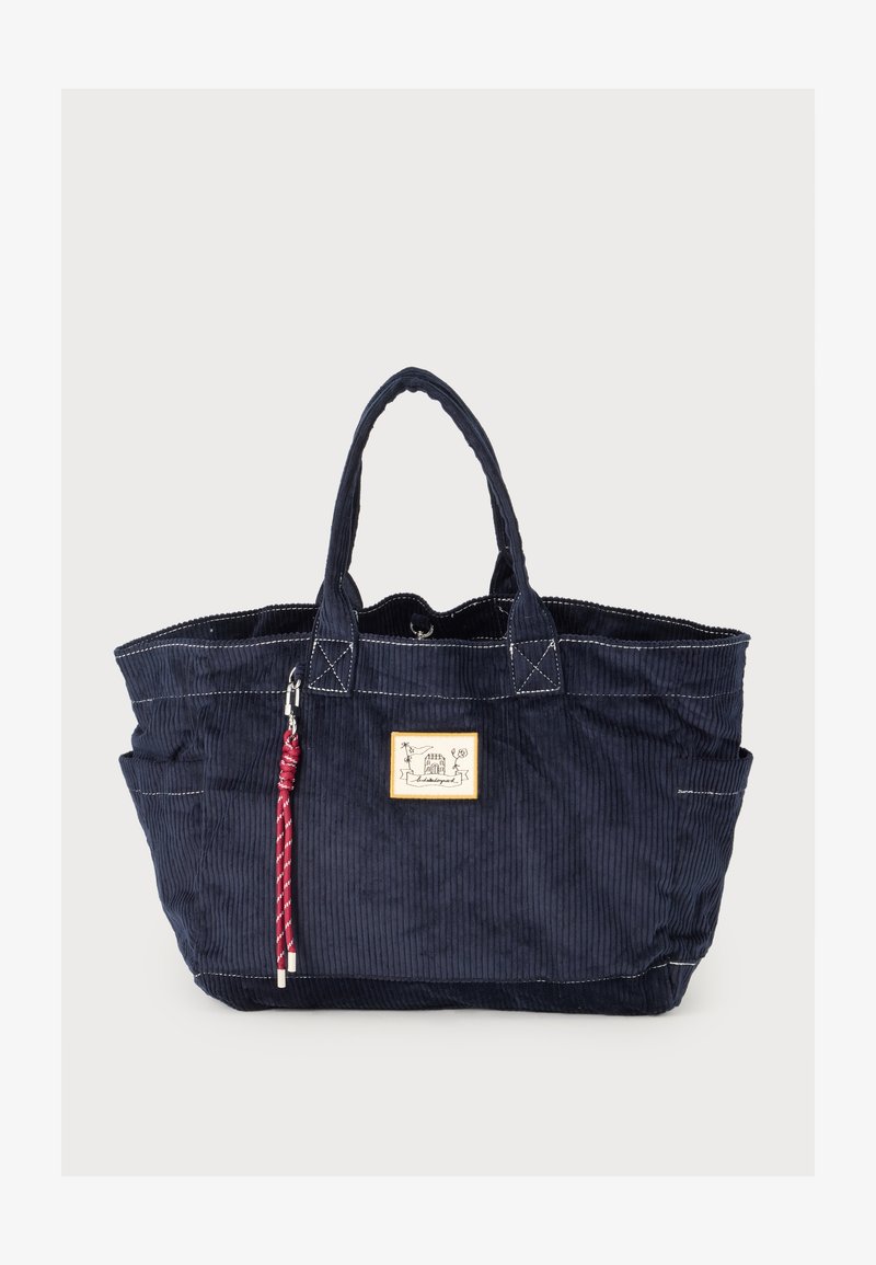 Sac cabas en velours côtelé bleu marine avec deux anses, coutures blanches, logo frontal en patch et porte-clés tressé rouge suspendu à une anse.