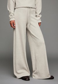 Ljust grå vida byxor i ribbat tyg, med justerbar dragsko i midjan och avslappnad passform. Kombineras med mörka skor.