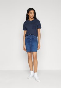 Navy cotton t-shirt with a textured pocket, paired with a fitted blue denim skirt. Model wears white high-top sneakers. Simple and casual look.