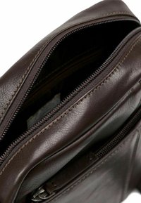 Bolso de cuero marrón con textura suave, que cuenta con un cierre de cremallera y detalles de costura visibles. Al abrirlo, se revela un forro interior negro.