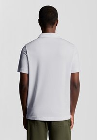 Weißes kurzärmliges Poloshirt mit klassischem Kragen. Weiche Textur, gerader Saum und lockere Passform. Trägt man mit olivgrünen Hosen.
