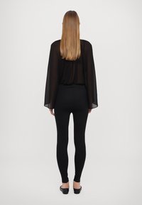 Czarna prześwitująca bluzka z szerokimi rękawami, zestawiona z dopasowanymi czarnymi legginsami. Gładka faktura, minimalistyczny design i subtelny, swobodny krój.