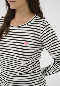 Top cu mâneci lungi, dungi alb-negru, cu decolteu rotund și un mic patch în formă de inimă roz pe piept. Material moale, croială casual.