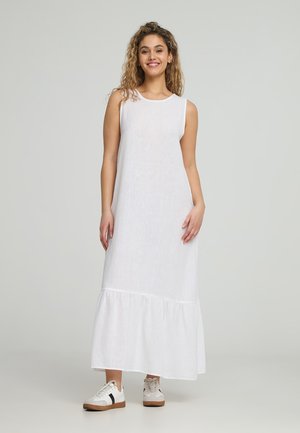 Abito maxi in lino bianco con scollo rotondo e design senza maniche, caratterizzato da un orlo a strati con volants. Indossato con sneaker casual.