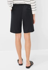 Pantaloni corti neri con vita elasticizzata, dotati di due tasche posteriori. Il tessuto sembra liscio con una vestibilità comoda, con orlo all'altezza della metà della coscia.