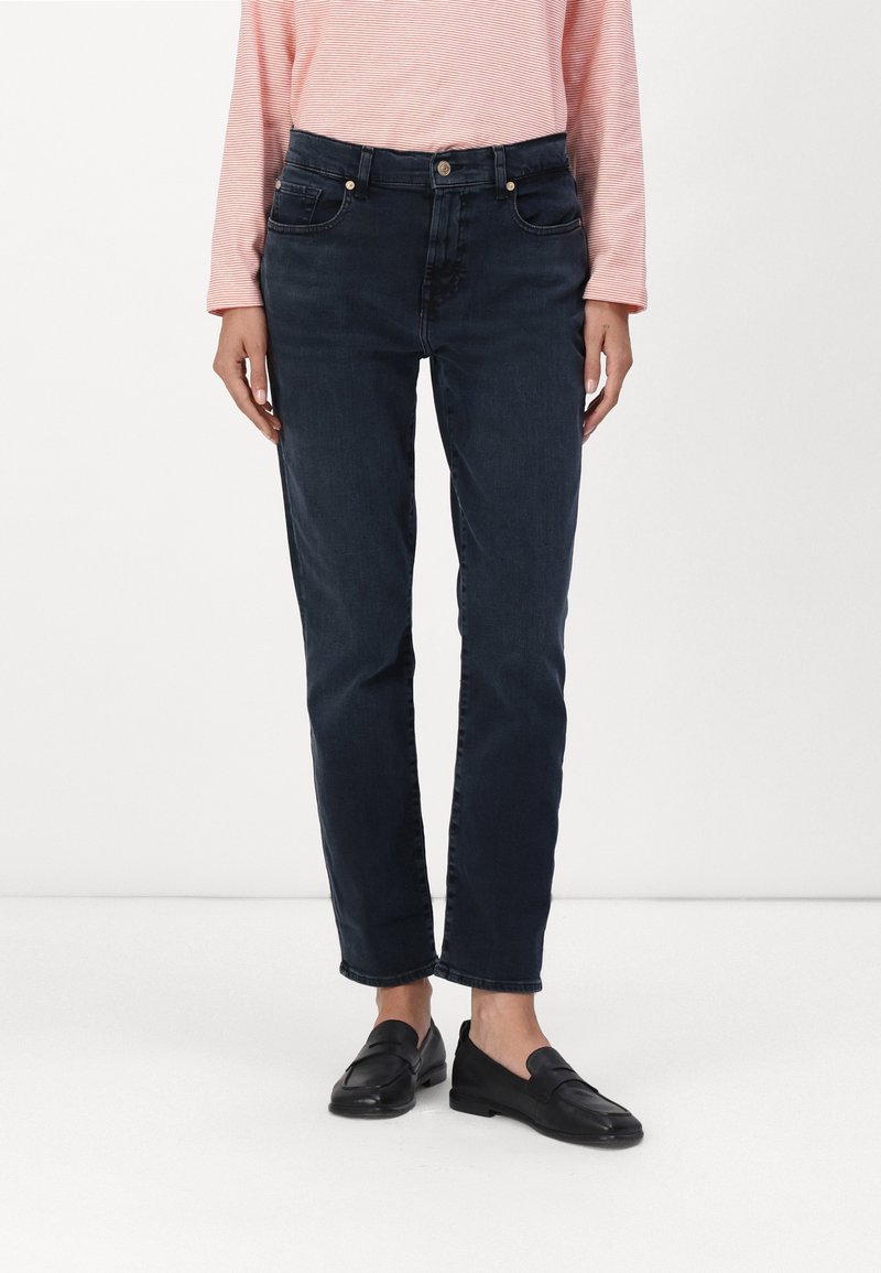 Jeans de denim oscuro con corte recto, que presentan un diseño de cinco bolsillos y un sutile bordado. Combinados con mocasines negros y una camisa de manga larga a rayas rosas.