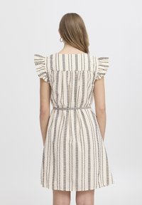 Abito beige a maniche corte con strisce verticali nere, dettagli arricciati sulle spalle, vita aderente e gonna svasata.