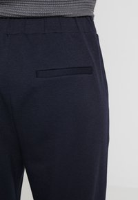 Granatowe spodnie uszyte z miękkiego materiału, o luźnym kroju. Posiadają płaską tylną kieszeń wzdłuż szwu oraz elastyczny pas.