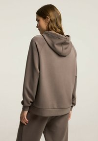 Kaptur z gładkiego, stonowanego koloru taupe. Posiada gładką teksturę, luźny krój oraz ribbowe mankiety. Prosty design bez widocznych logo.